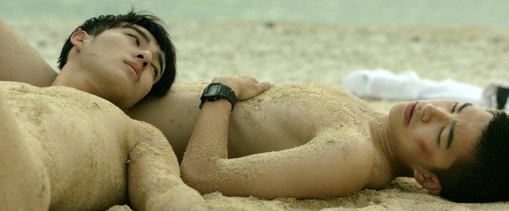 The two boys lying on the beach, naked and covered in sand, with Jia-han leaning against Birdy.