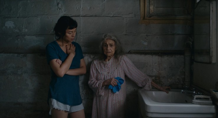 Olivia (left) and Olga (right) standing in front of a sink, with Olivia speaking to Olga as Olga looks very confused holding a washcloth.